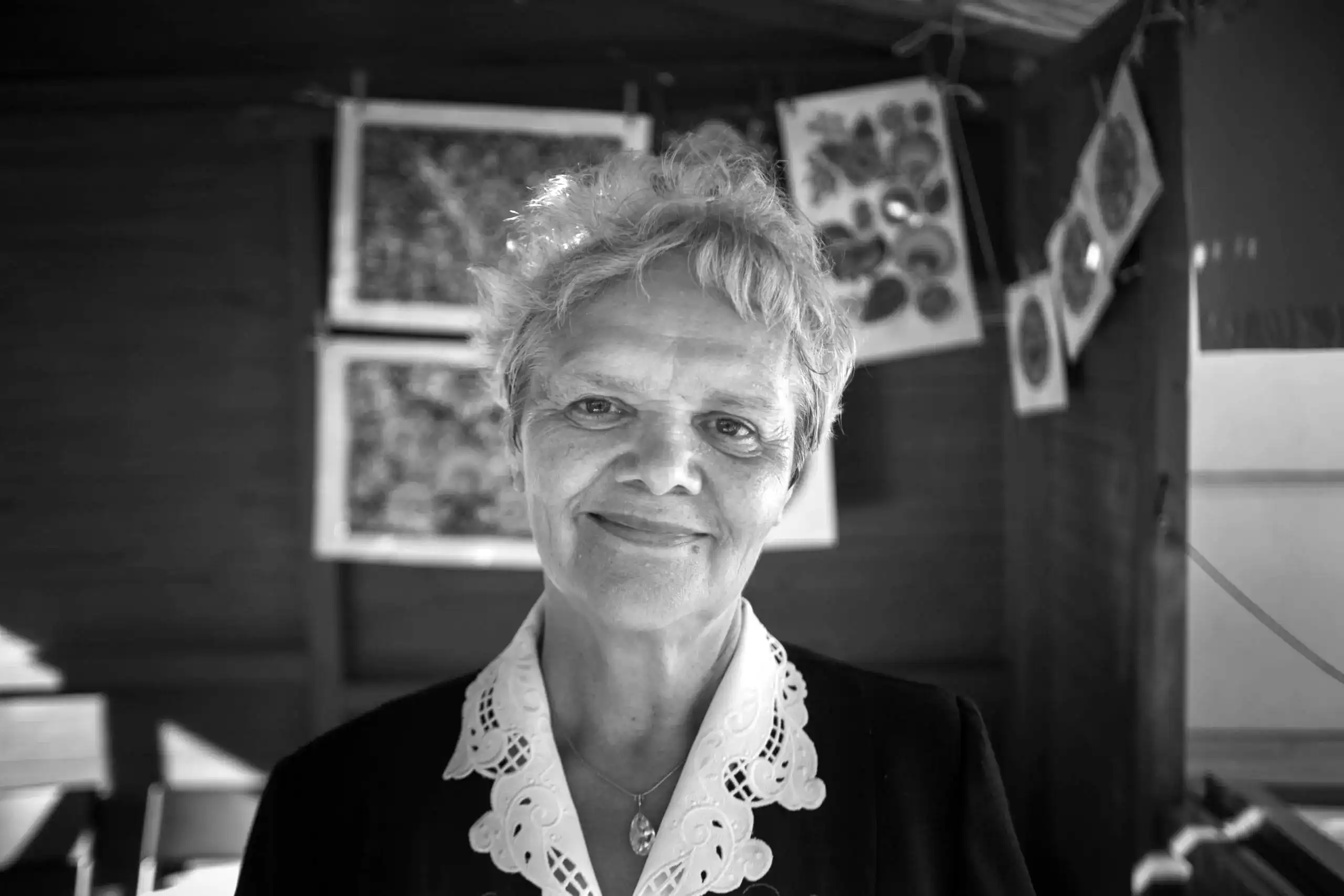 Portret twórczyni. Delikatnie uśmiechnięta, starsza kobieta pozuje na tle swoich wycinanek.