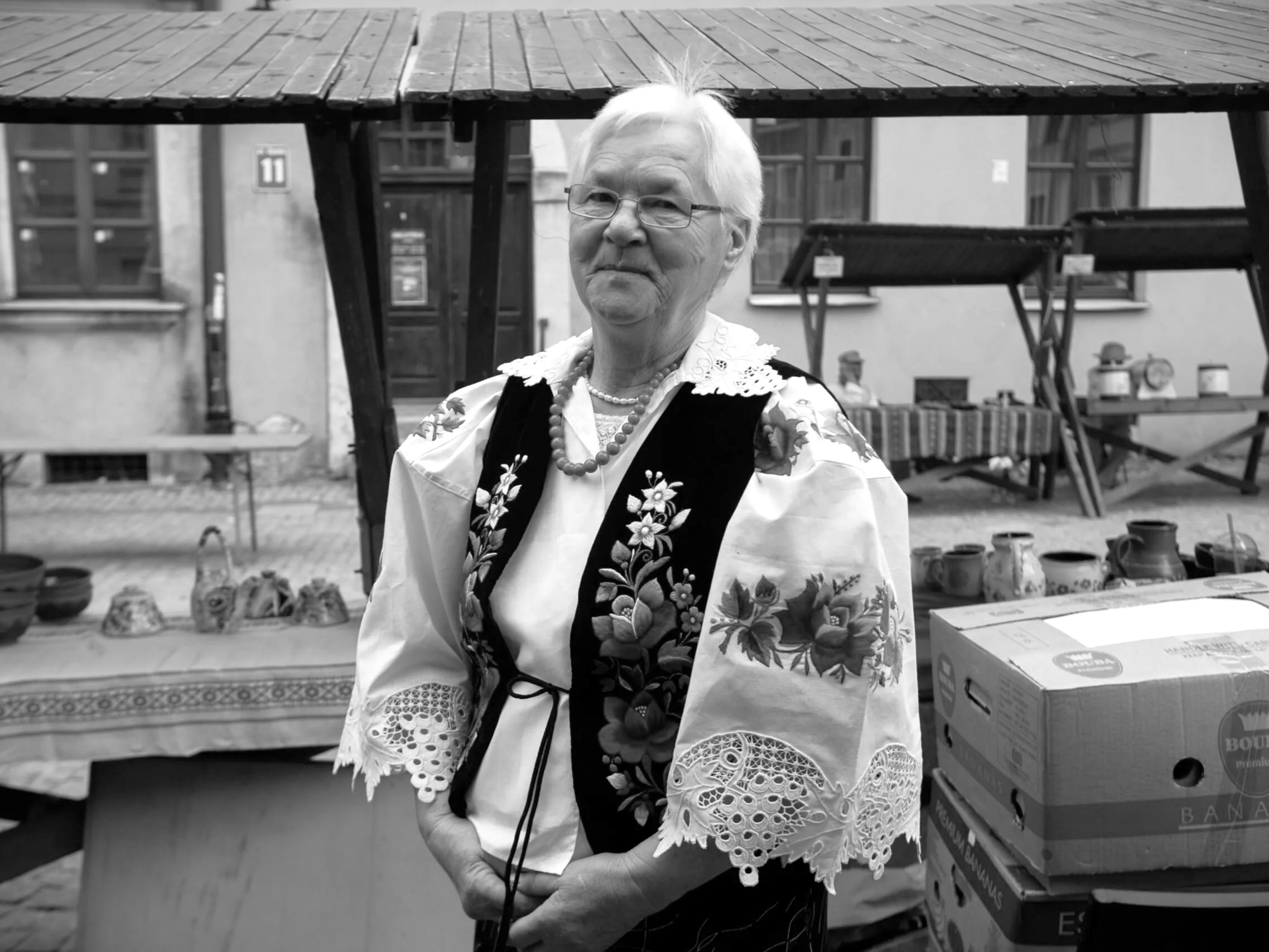 Czarno-biały portret starszej twórczyni. Kobieta jest w białej, haftowanej w kwiaty bluzce i gorsecie.