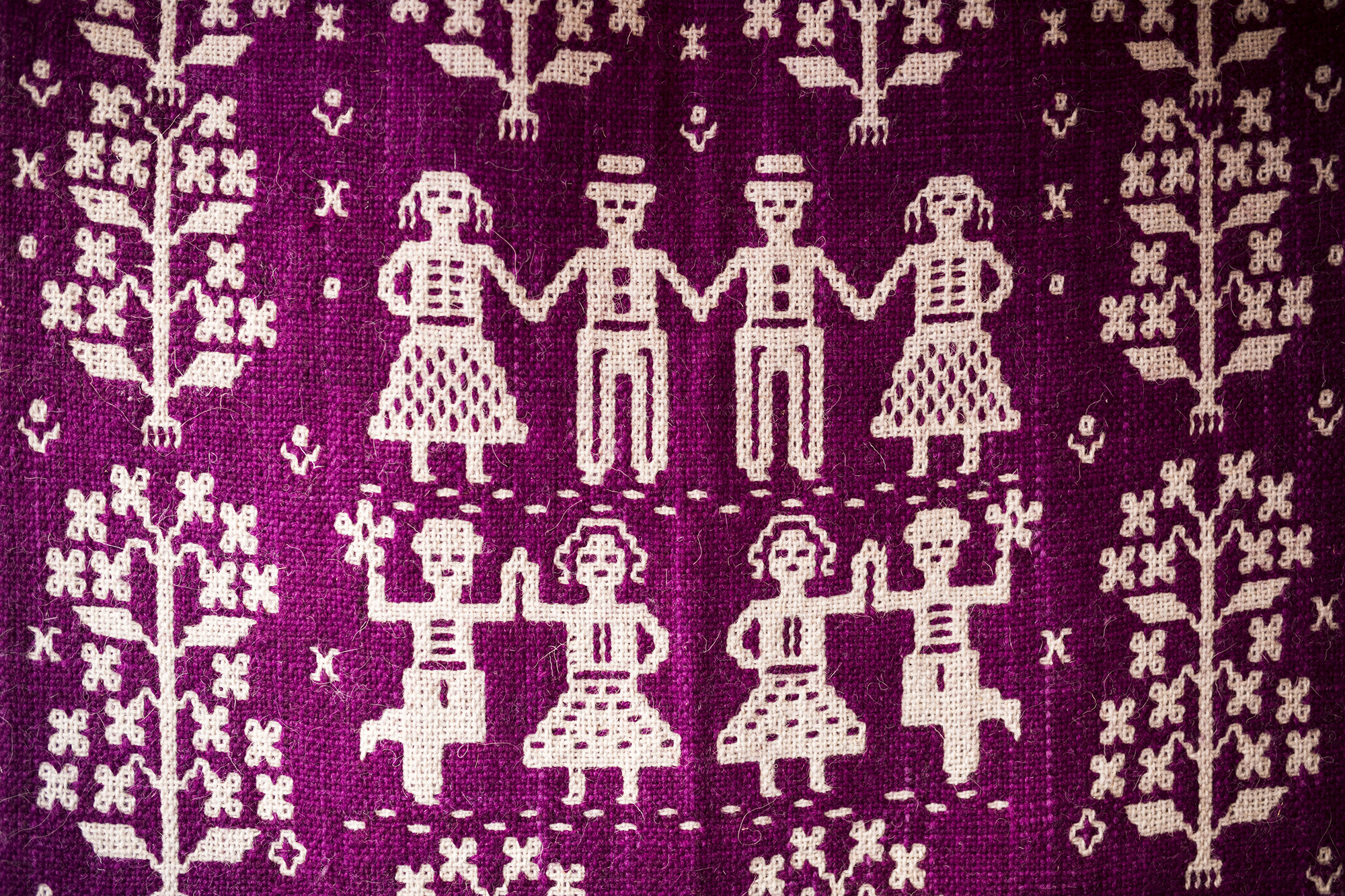 Tkanina dwuosnowowa. Na ciemniejszym różowym tle widać biały wzór przedstawiający schematyczne postaci tańczących ludzi.