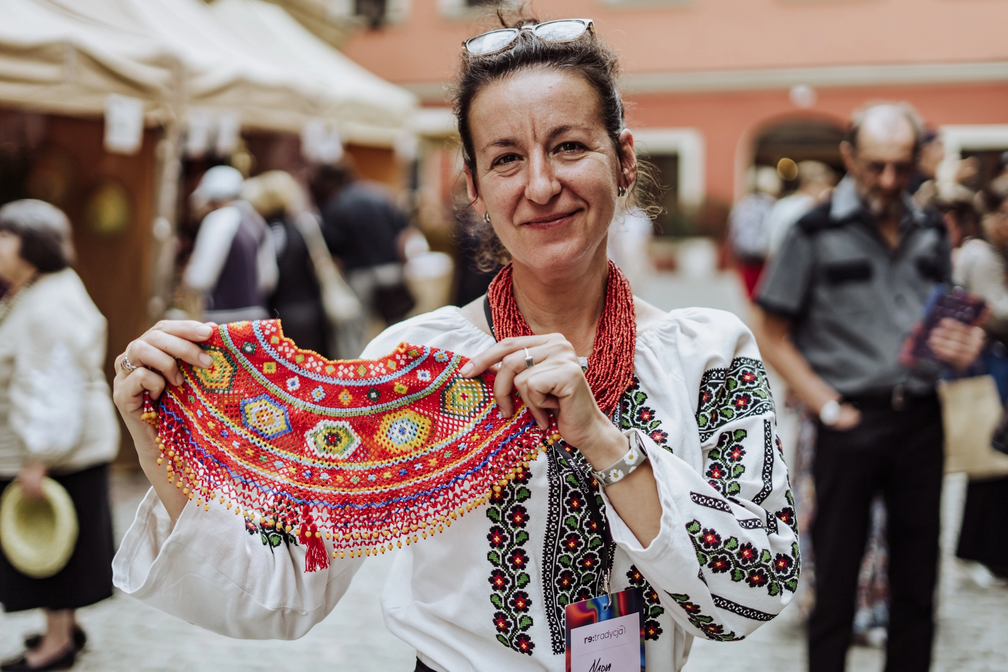 Portret twórczyni. Kobieta trzyma w rękach naszyjnik wypleciony z małych koralików.