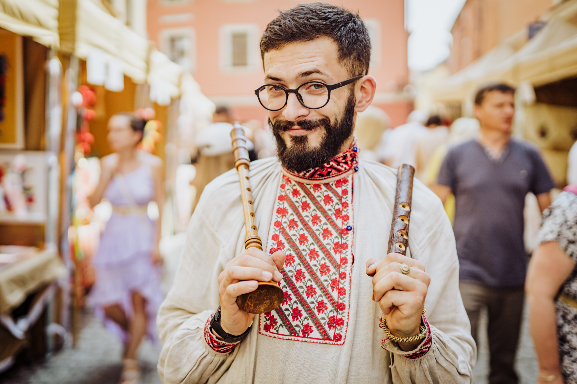 Mężczyzna w koszuli ze wzorem ludowym trzyma w ręce dwa flety.