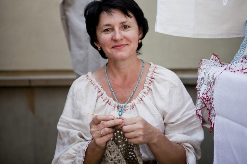[Kobieta stoi na swoim stoisku z tradycyjnym rękodziełem.]