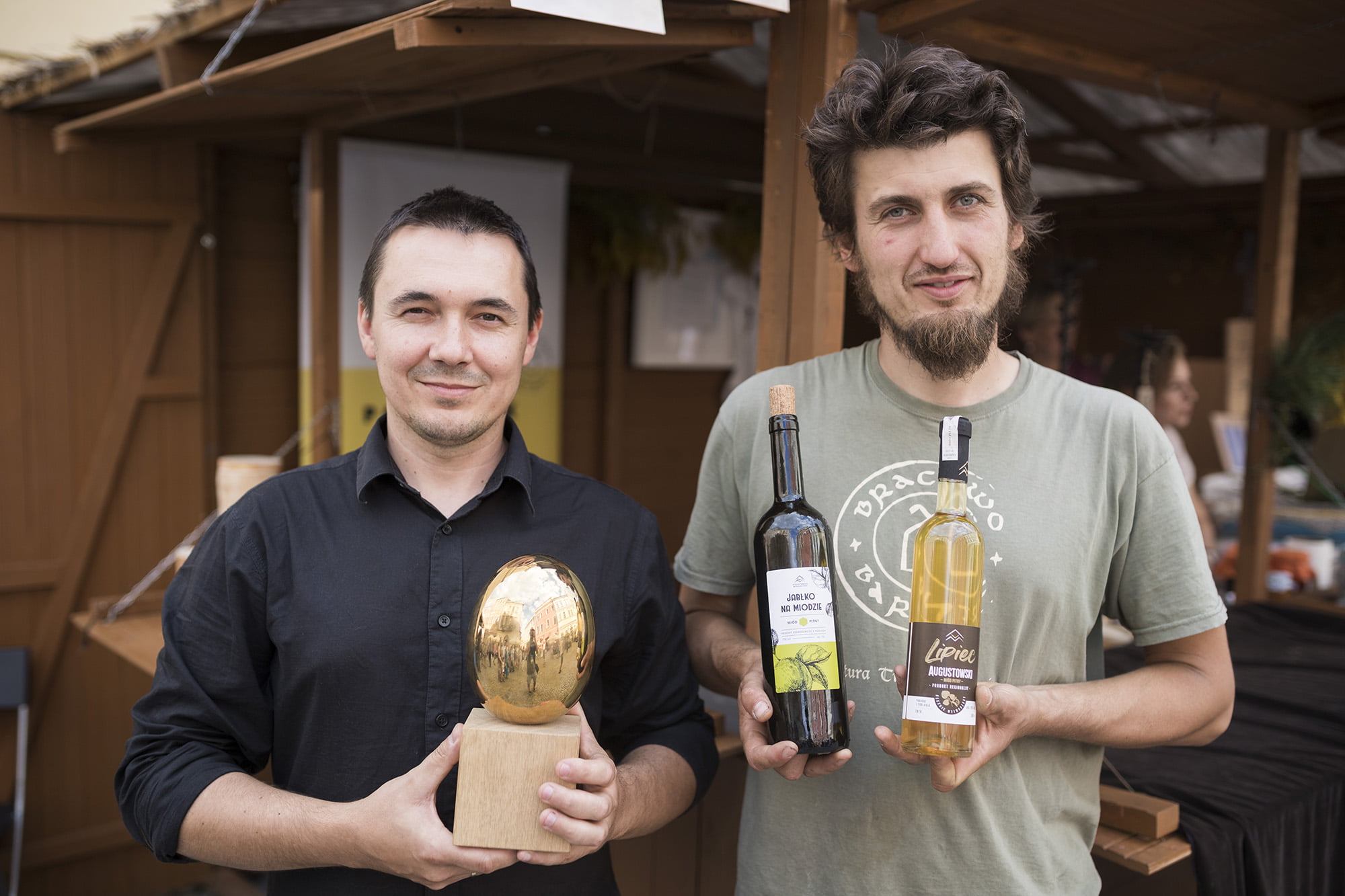 [Dwóch młodych mężczyzn, jeden w ręku trzyma dwie butelki, drugi złote jajo.]