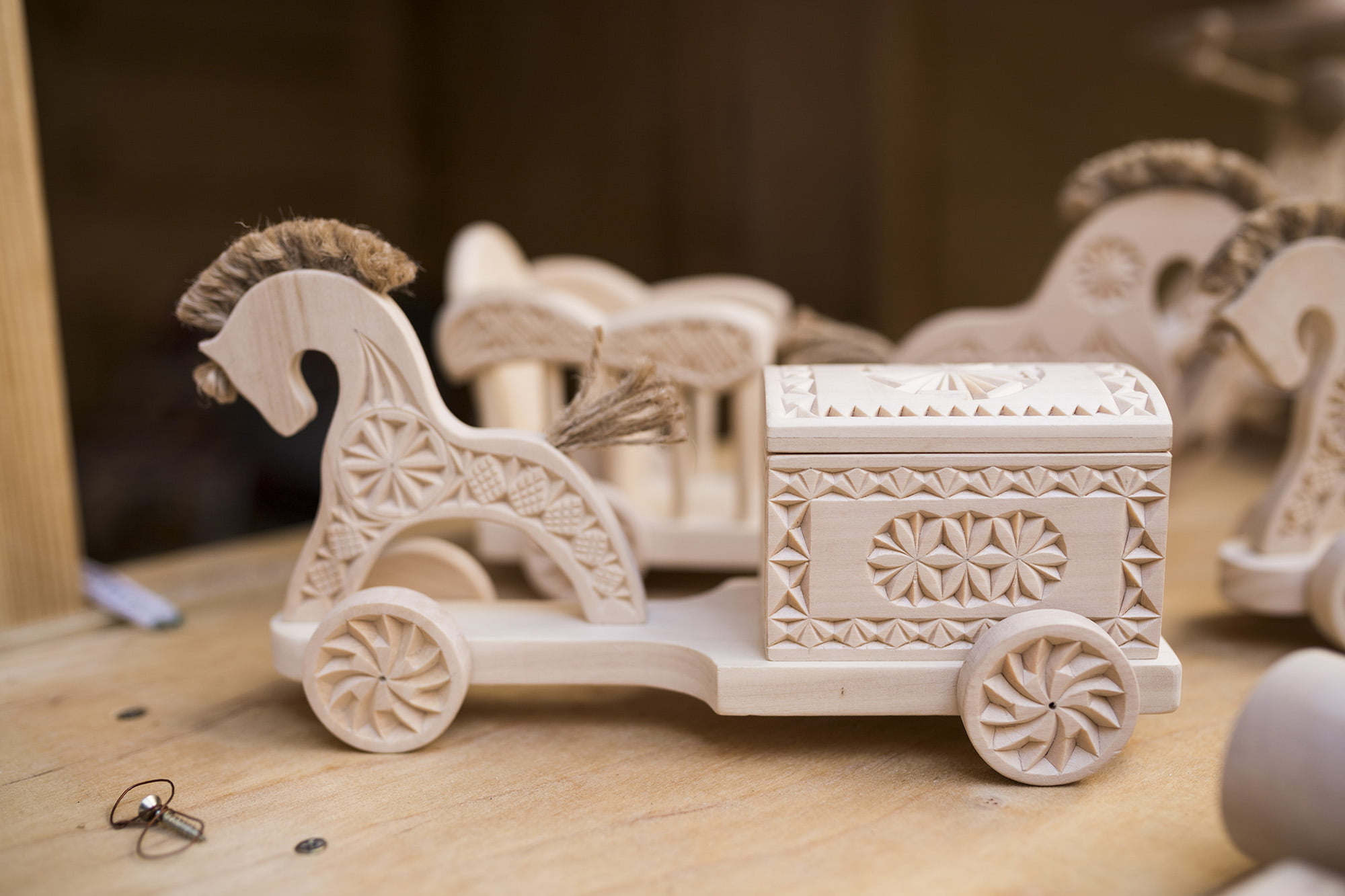 [Zabawki drewniane w kształcie małych koni, wozu i kuferka. Wszystkie elementy zdobione pięknymi wzorami.]