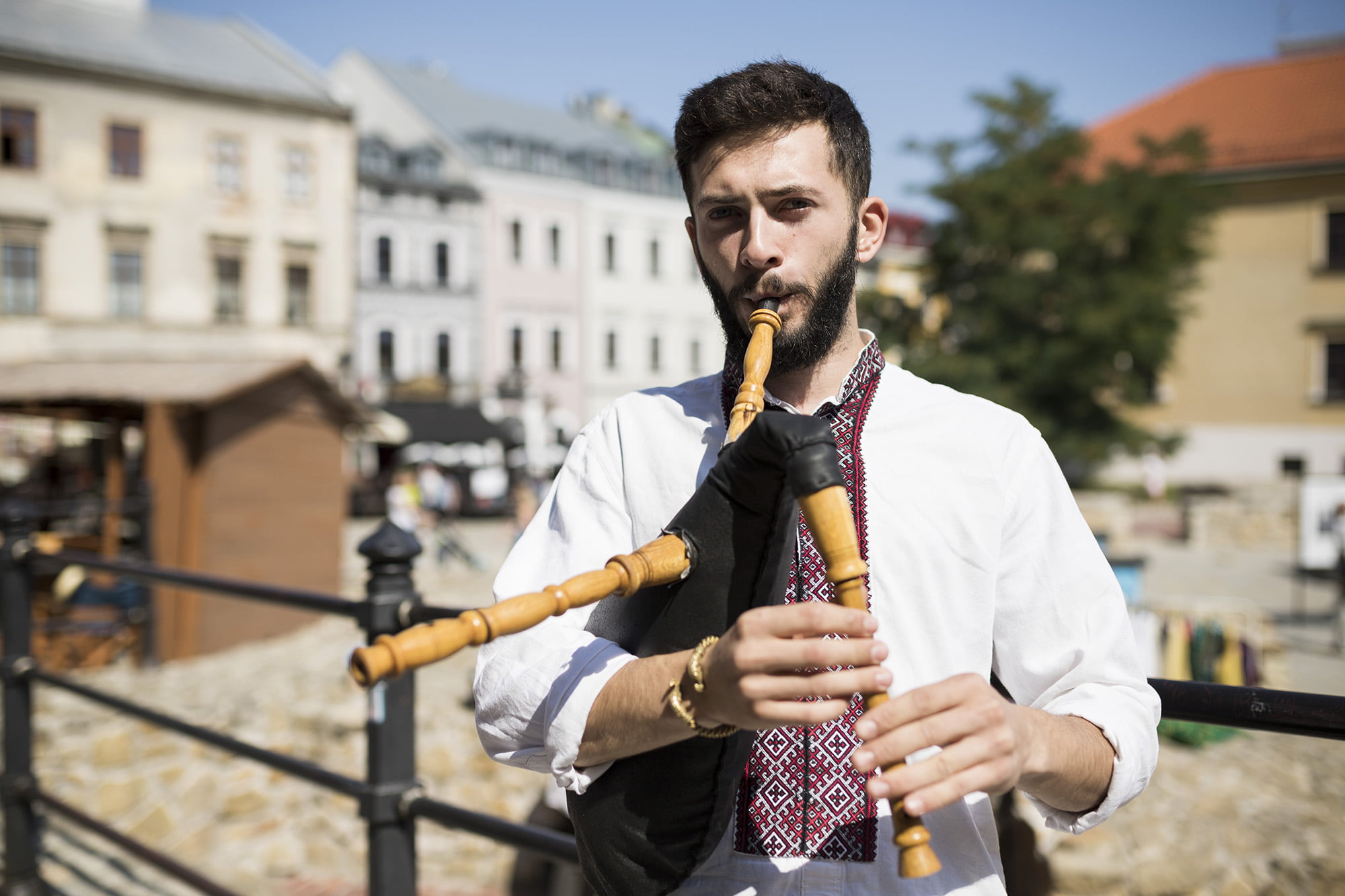 [Młody mężczyzna w stroju ludowym, stoi na Placu Po Farze i gra na instrumencie tradycyjnym.]