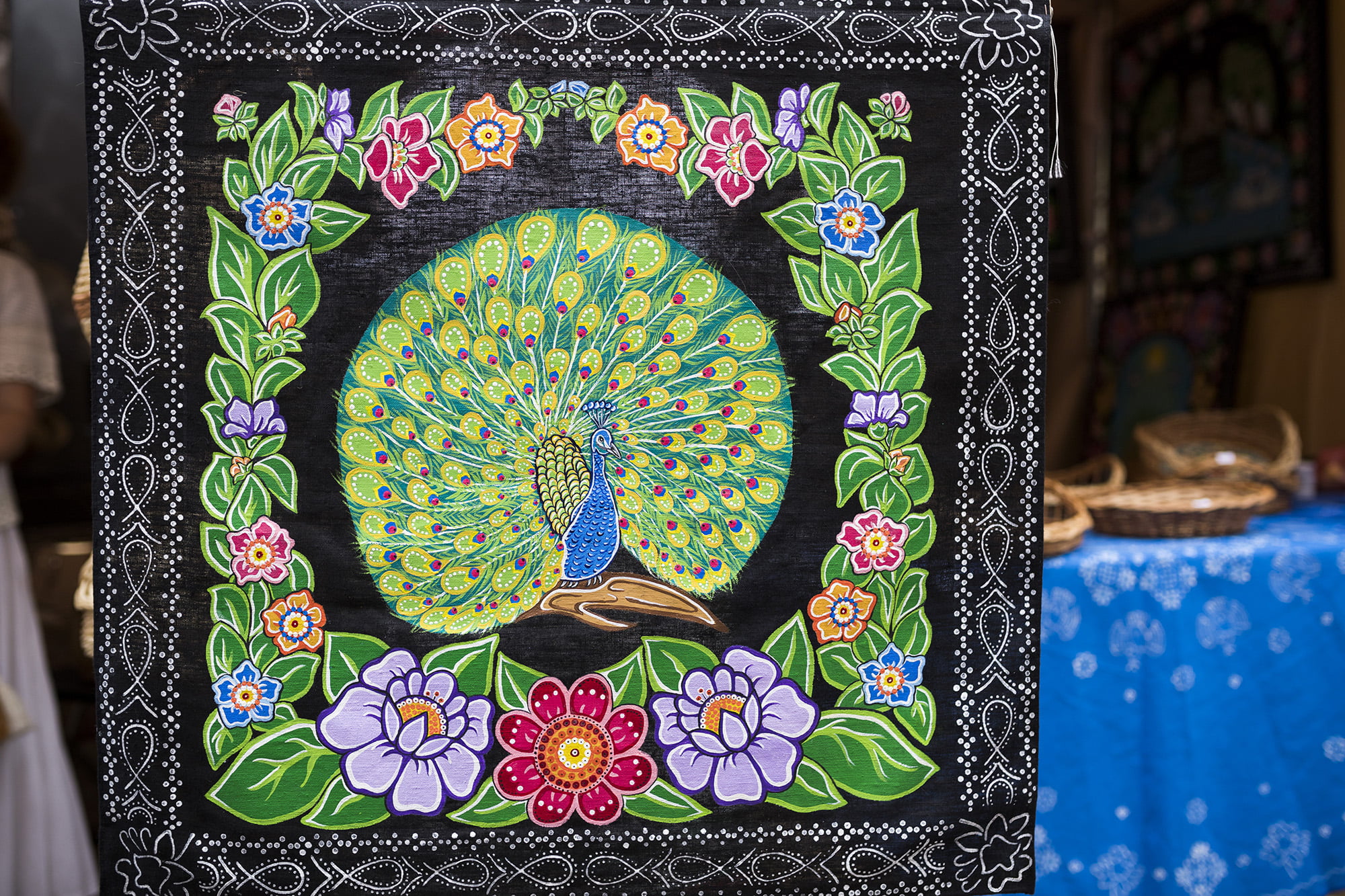 [Zbliżenie. Dekoracyjna tkanina przedstawiająca pawia otoczonego kolorowymi kwiatami i zielonymi liśćmi na czarnym tle.]
