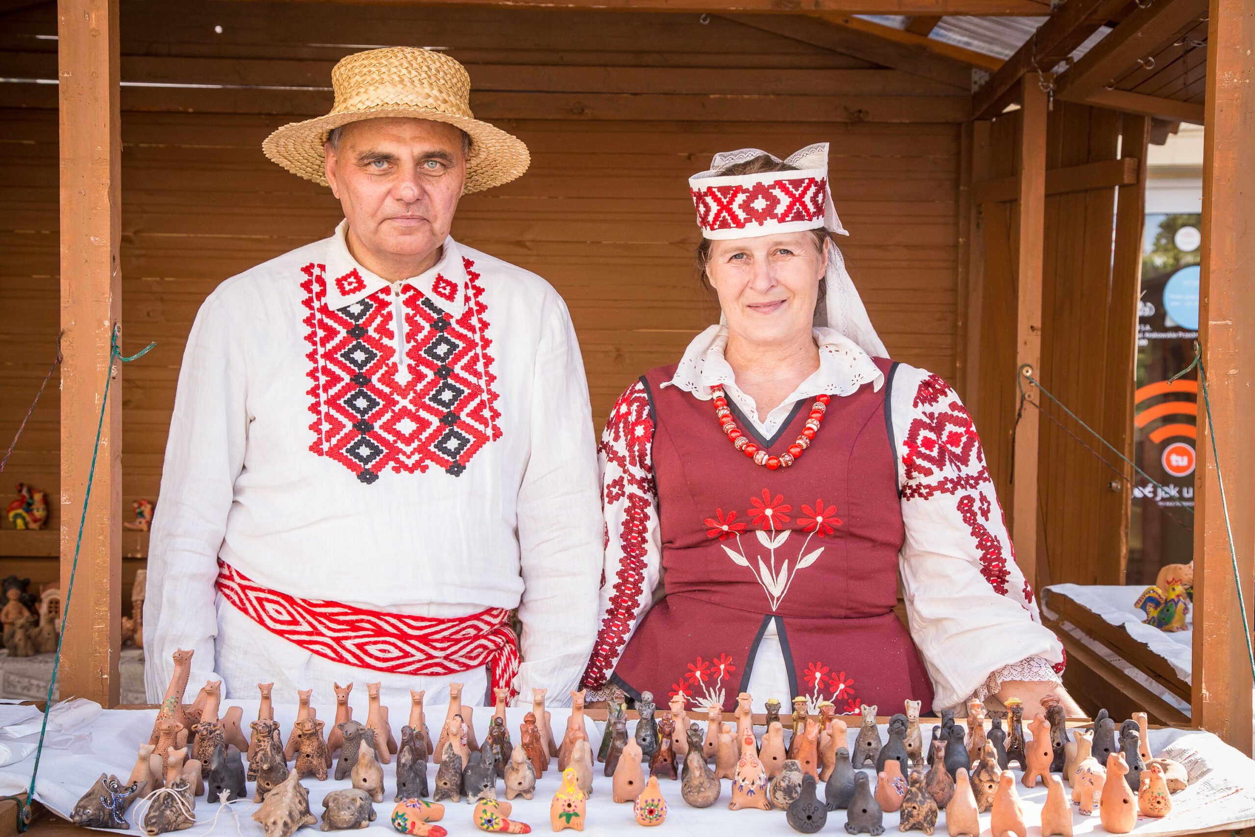 [Mężczyzna i kobieta ubrani w stroje tradycyjne. prezentują wyroby z ceramiki.]
