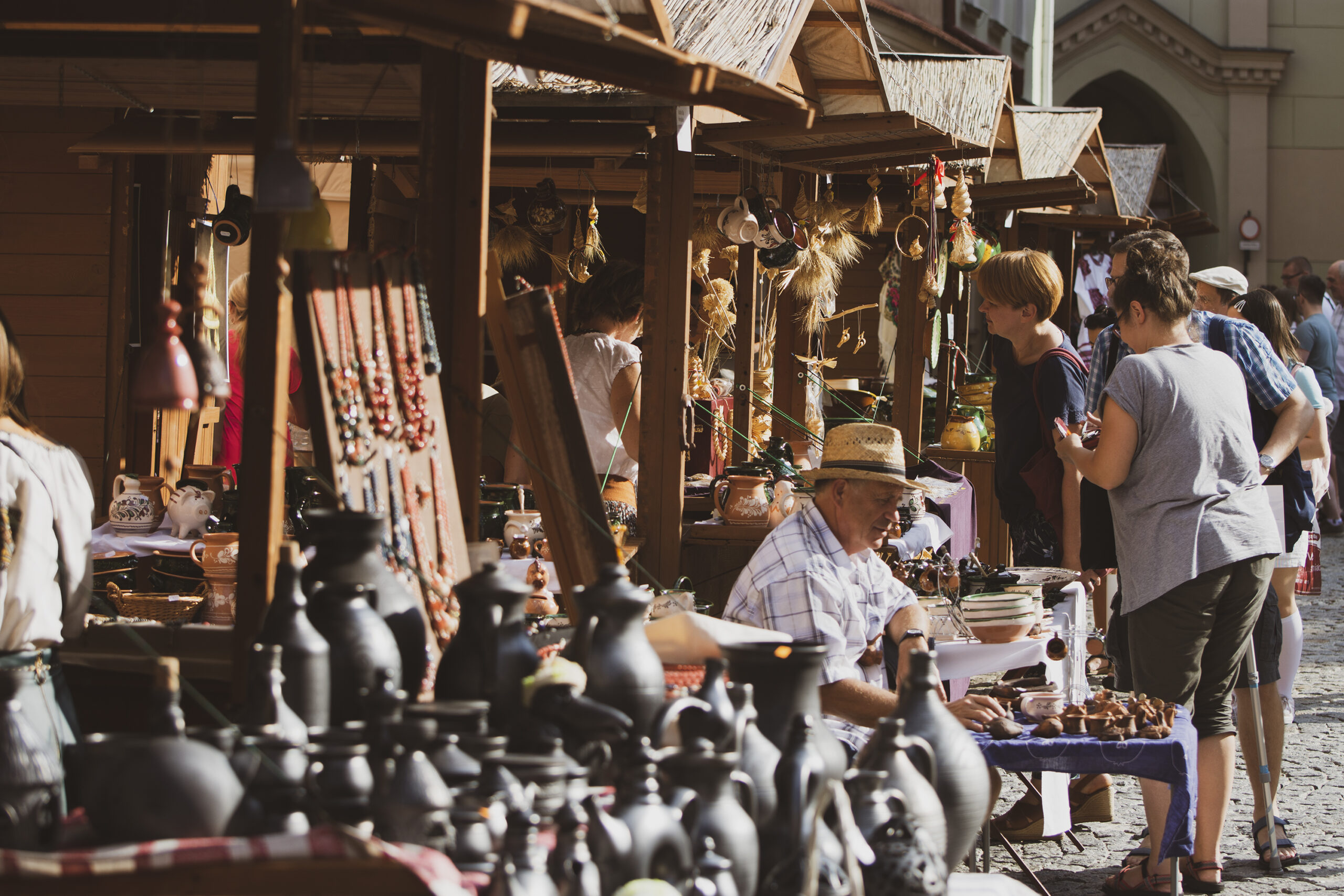 jarmark rzemieślniczy stragany - drewniane stragany z wyrobami rzemieslników , ludzie przyglądający się wyrobom
