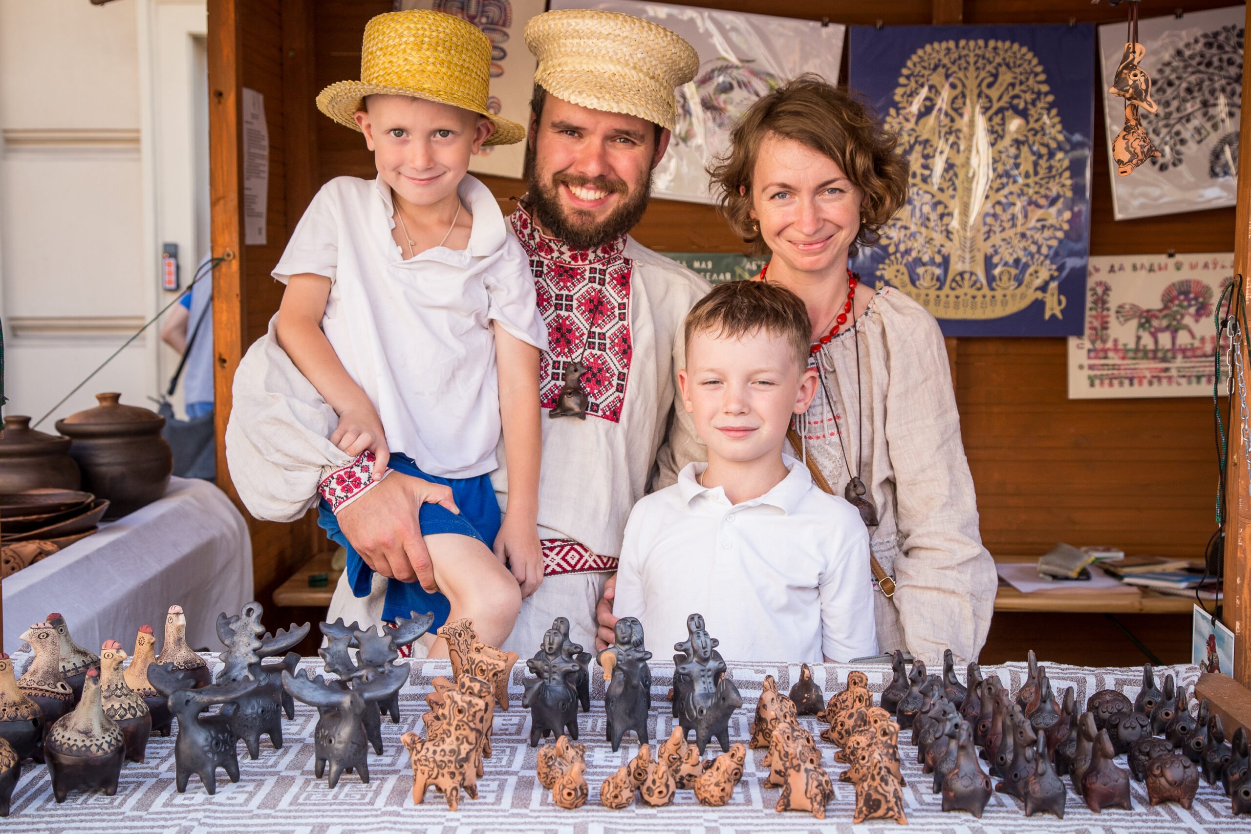 A smiling family consisting of a man, woman and two little boys are presenting their products in a wooden booth
