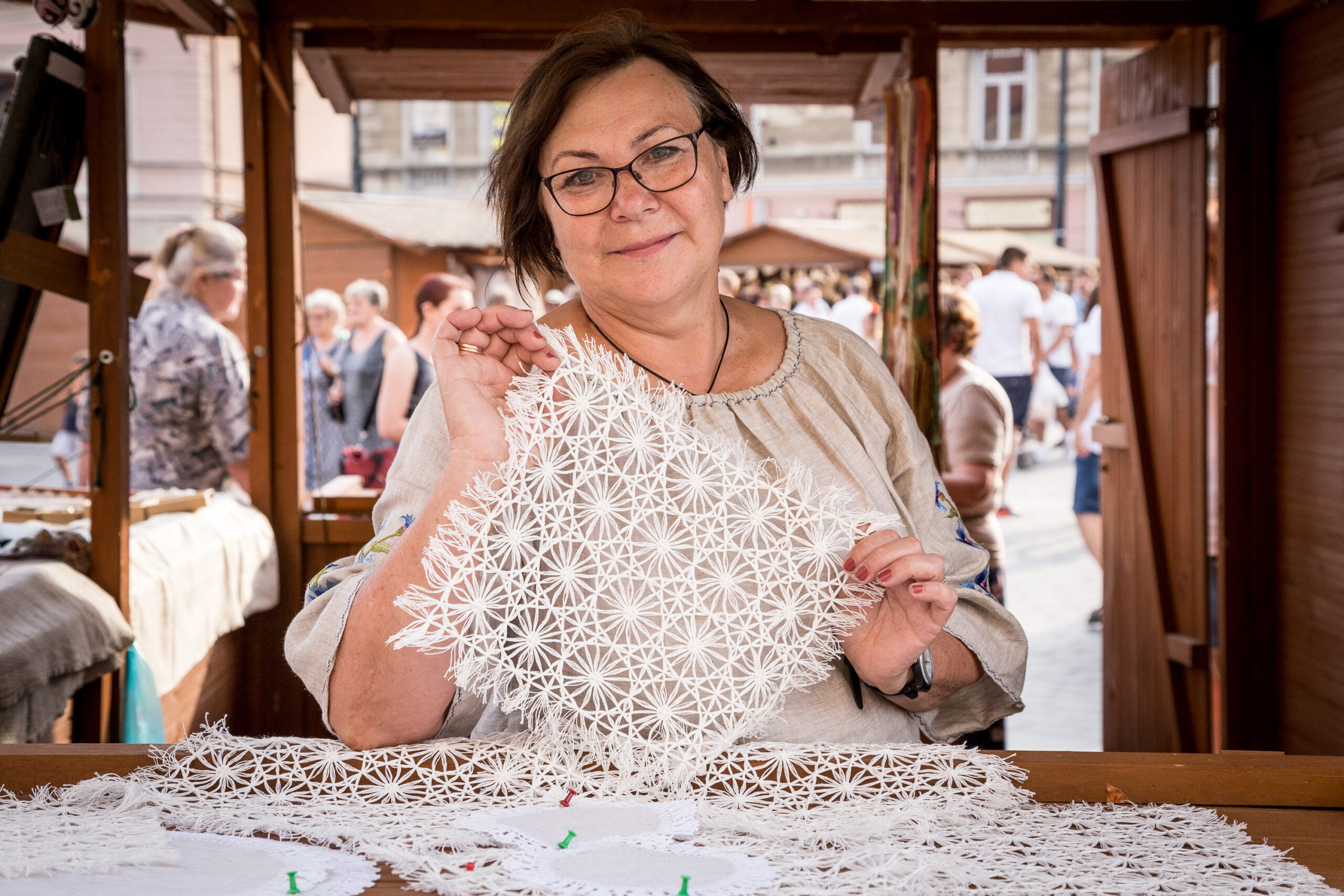 [Uśmiechnięta kobieta prezentuje białą ozdobną koronkę.]