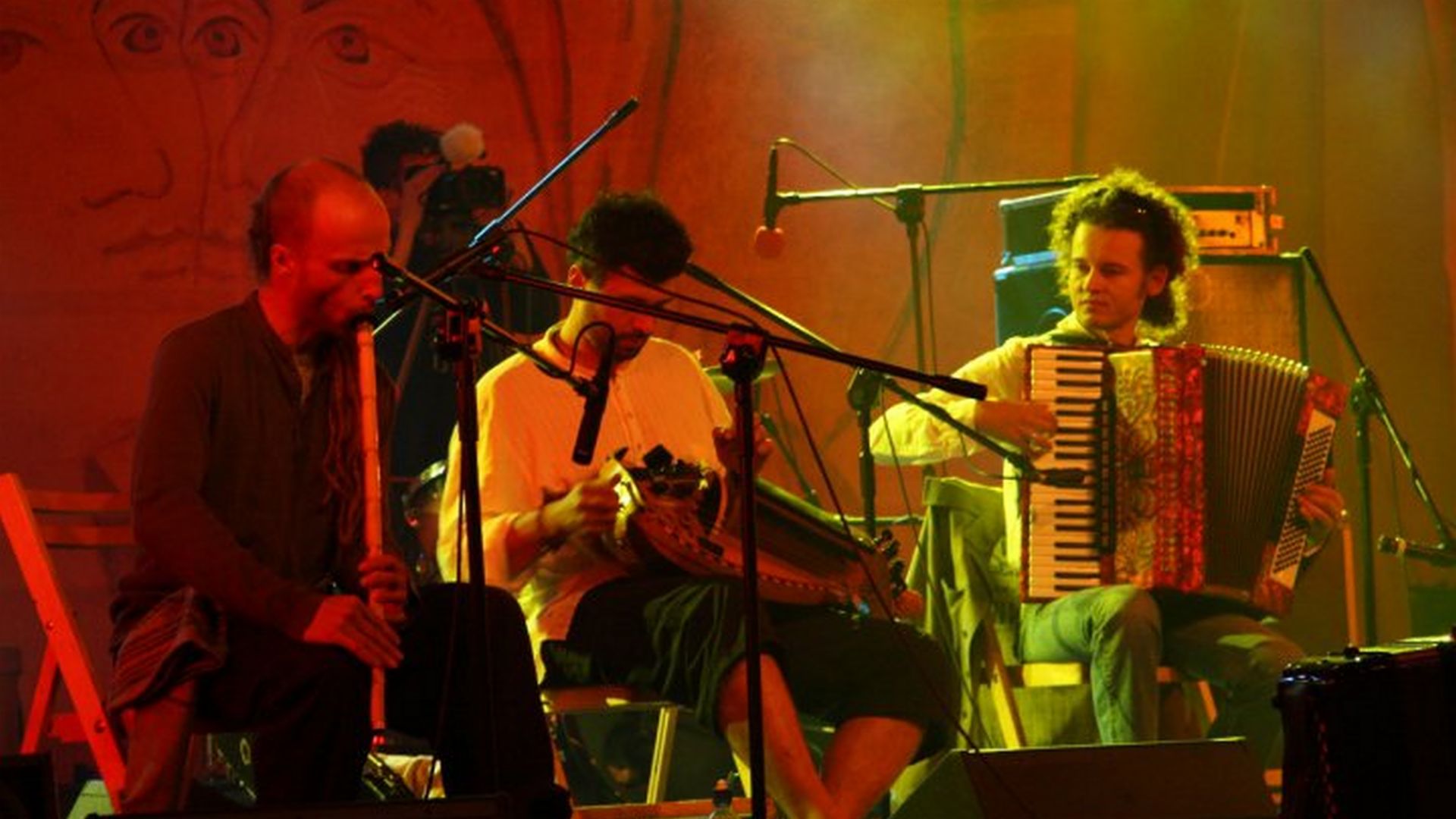 [Trzej mężczyźni grają na tradycyjnych instrumentach. Siedzą na scenie koncertowej. Przed nimi mkrofony na statywach.]