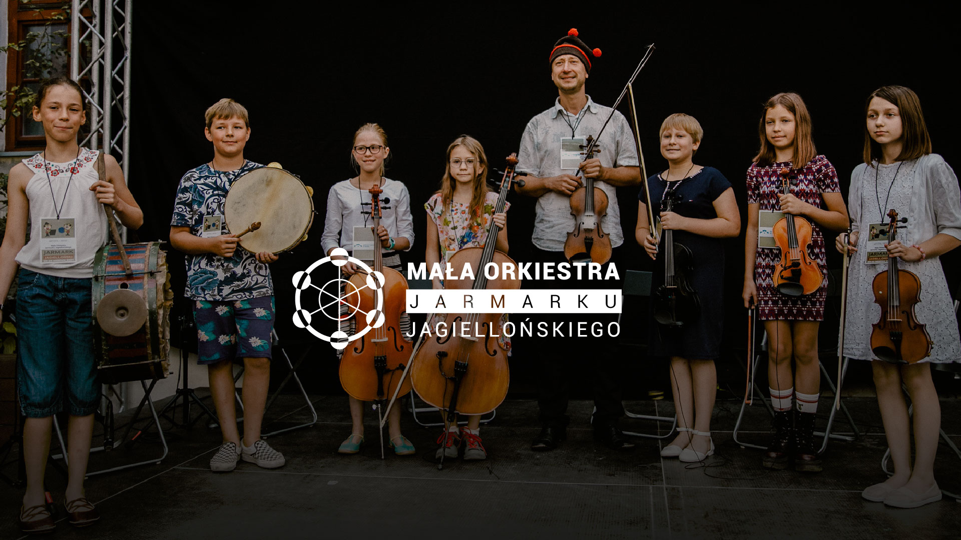 Na scenie zespół grający na instrumentach tradycyjnych. Na środku logo Małej Orkiestry Jarmarku Jagiellońskiego.