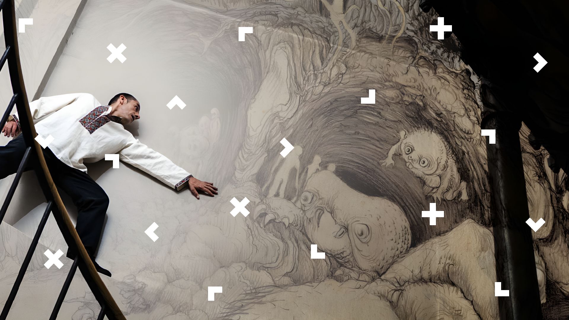 Mężczyzna stoi na podwyższeniu i opiera się o ścianę. Są na niej narysowane stwory z mitologii słowiańskiej.