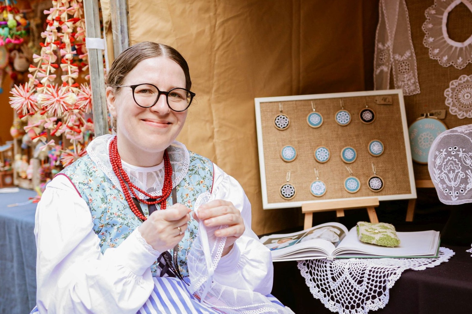 Portret twórczyni. Kobieta w stroju ludowym i czerwonych koralach. Haftuje.