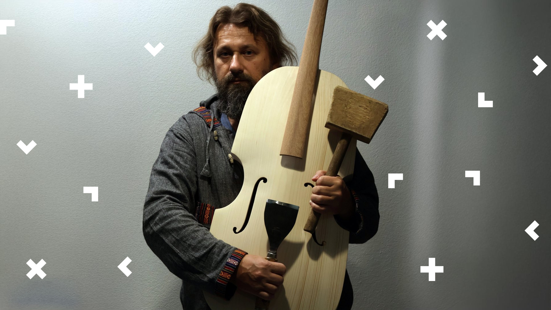 Mężczyzna z długimi włosami i brodą trzyma w ręce drewniany instrument.