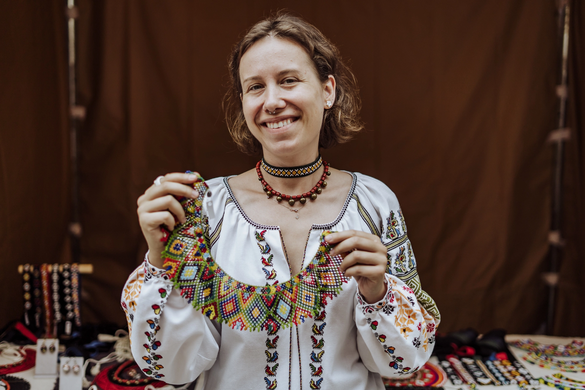 Portret twórczyni. Młoda kobieta trzyma w rękach naszyjnik utkany z drobnych koralików.