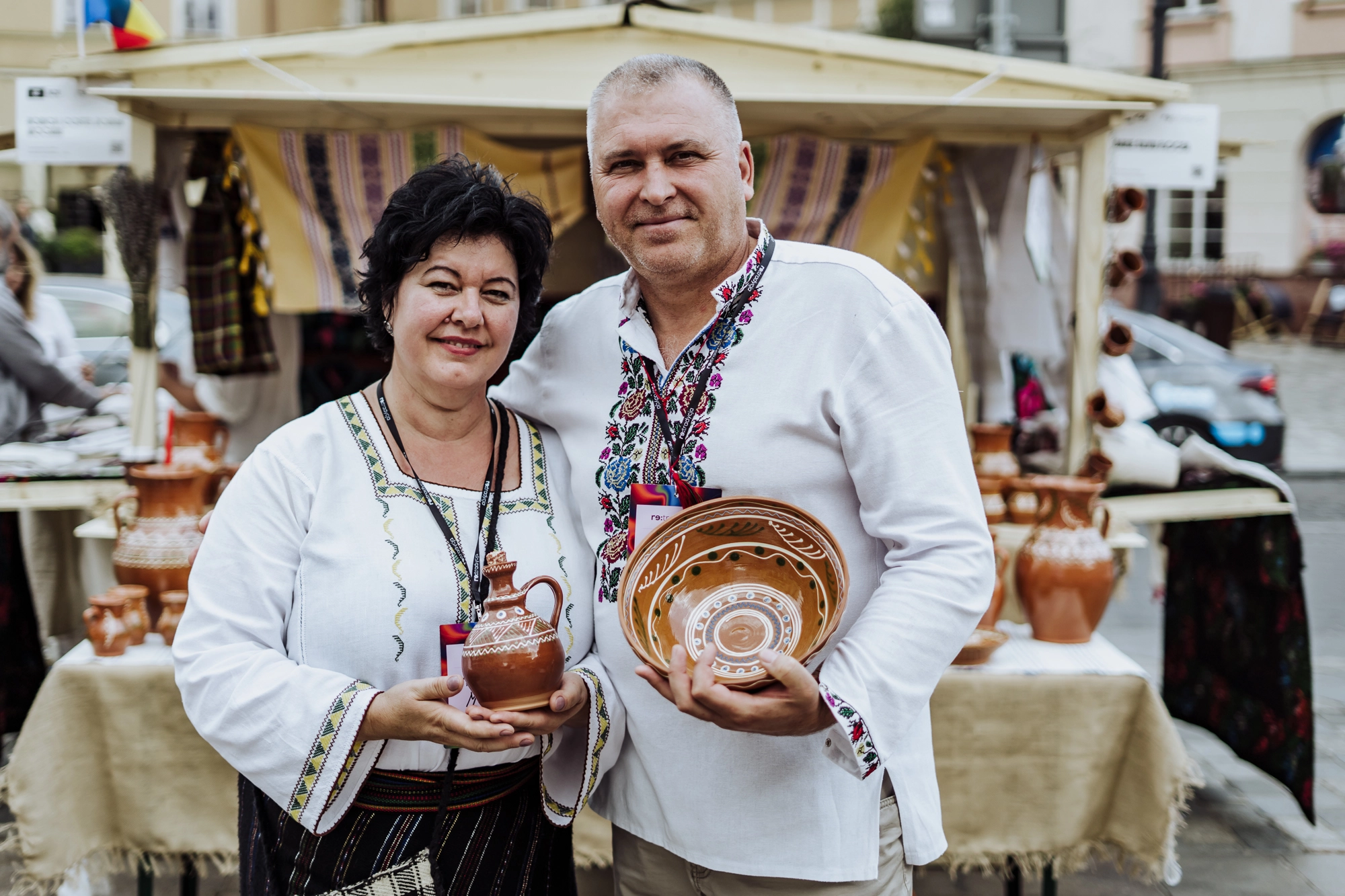 Portret twórców. Kobieta i mężczyzna trzymają w rękach gliniany dzbanek i misę. Naczynia dekorowane delikatnym, białym wzorem.