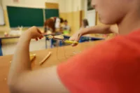 Zdjęcie. Chłopiec przycina czerwoną nić, którą związana jest słomiana miotełka.