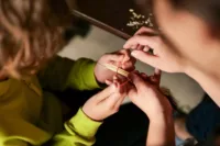 Zdjęcie. Dłonie rodzica dziecka. Zawiązują czerwoną nitkę na garstce słomy.