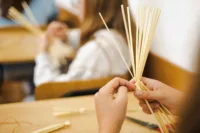 Zdjęcie. Dłonie. Jedna trzyma wiązkę słomy, a druga odgina pojedyncze słomki do dołu.