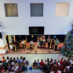 Widok na salę z góry. Widać scenę, na której są artyści i rzędy ławek, na których siedzą dzieci.