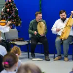 Kapela. Kobieta gra na skrzypcach. A dwaj mężczyźni na bębnie obręczowym i basach.