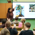 Dzieci siedzą w klasie. Prowadząca pokazuje zdjęcia podłaźniczek, czyli dawnych ozdób świątecznych.