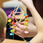 Dziecko trzyma w ręku słomianego pająka ozdobionego kolorową bibułą.