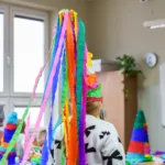 Dziewczynka biega po sali w spiczastej, kolorowej czapie, z której wychodzą długie wstążki bibuły.