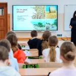 Dzieci siedzą w klasie. Prowadząca opowiada o słomie. Na tablicy wyświetla się prezentacja o słomie.