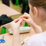 Dziewczynka zawiązuje czerwoną nitkę na garstce słomy.