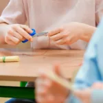 Dłonie dziecka przecinają nożyczkami czerwoną nić.