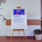 Pod ścianą stoi tablica opisująca, czym jest podłaźniczka.