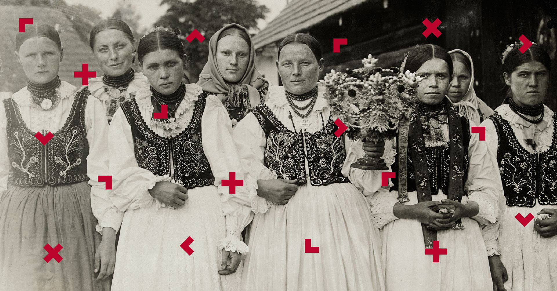 Grupa kobiet ma na sobie stroje ludowe. Jedna z nich trzyma bukiet kwiatów. Fotografia jest bardzo stara, czarno-biała.