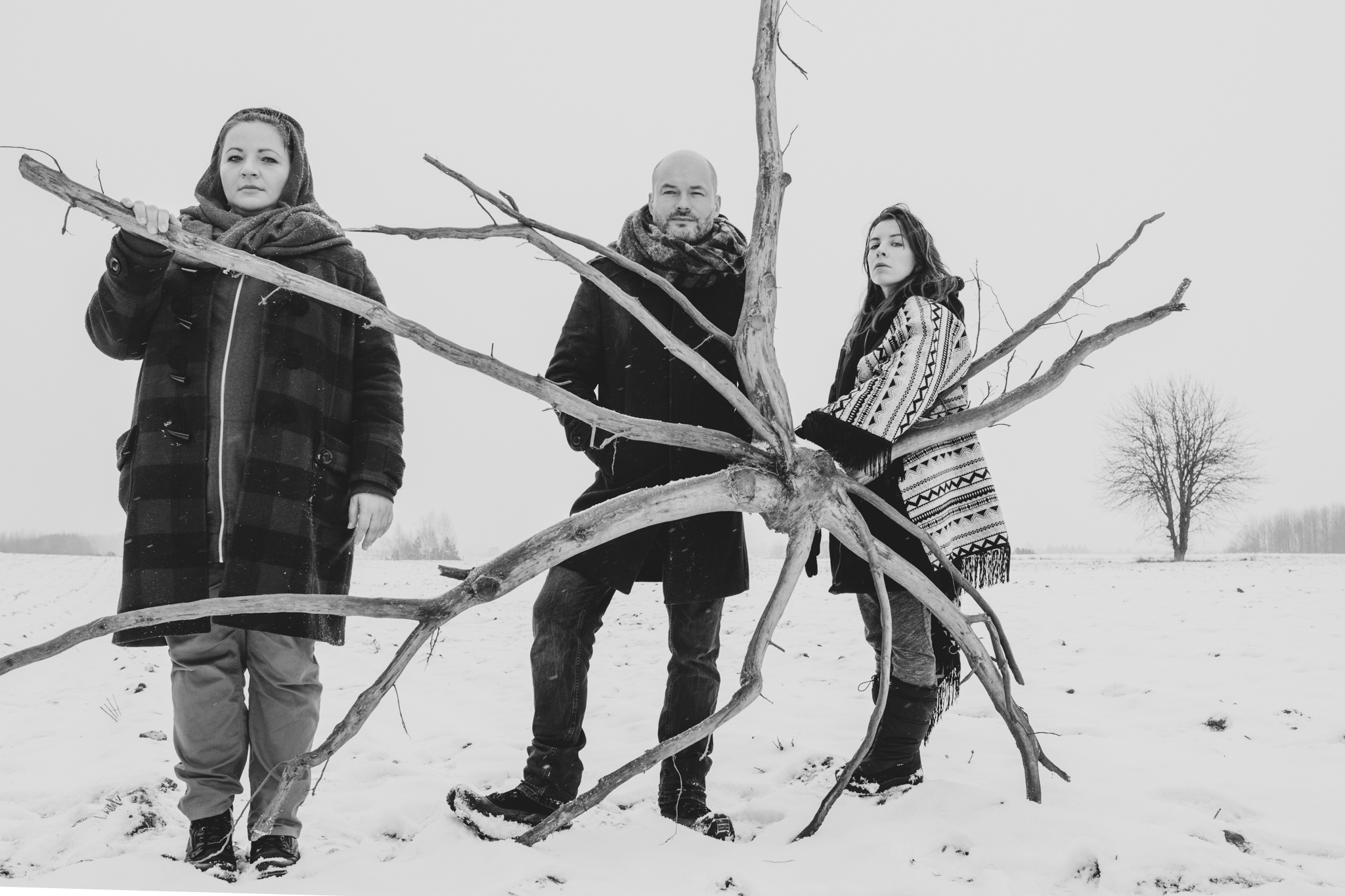 Troje muzykantów stoi na dworze przy drzewie. Jest zima i śnieg.
