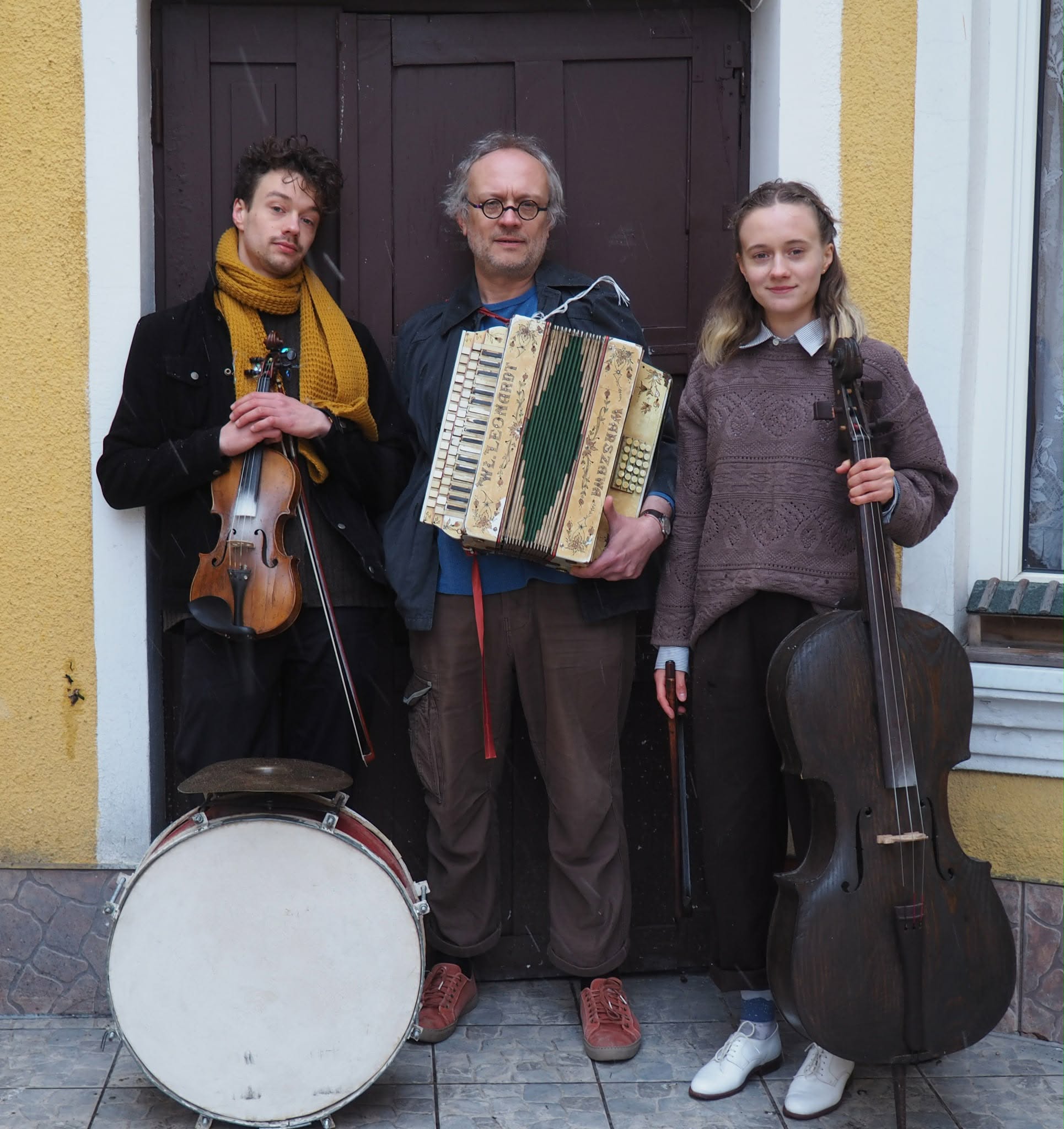 Dwaj mężczyźni i kobieta stoją przy drzwiach z instrumentami.
