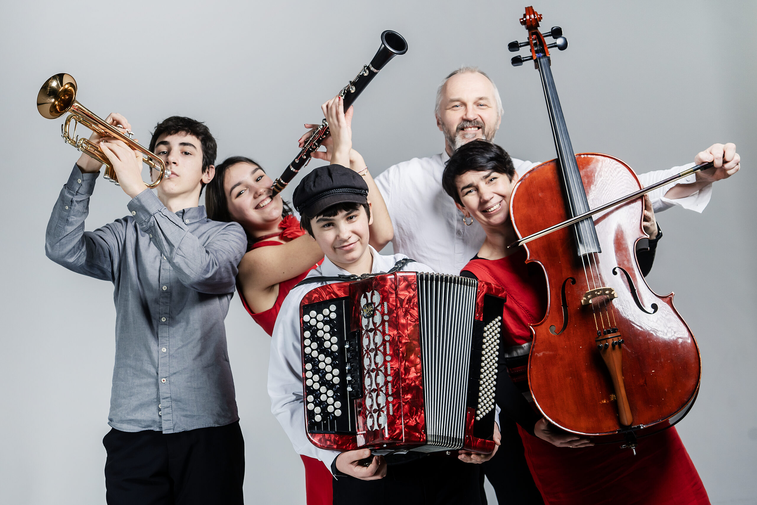Portret rodziny. Rodzice i trójka dzieci uśmiechają się i trzymają w dłoniach instrumenty - trąbkę, klarnet, akordeon i wiolonczelę.